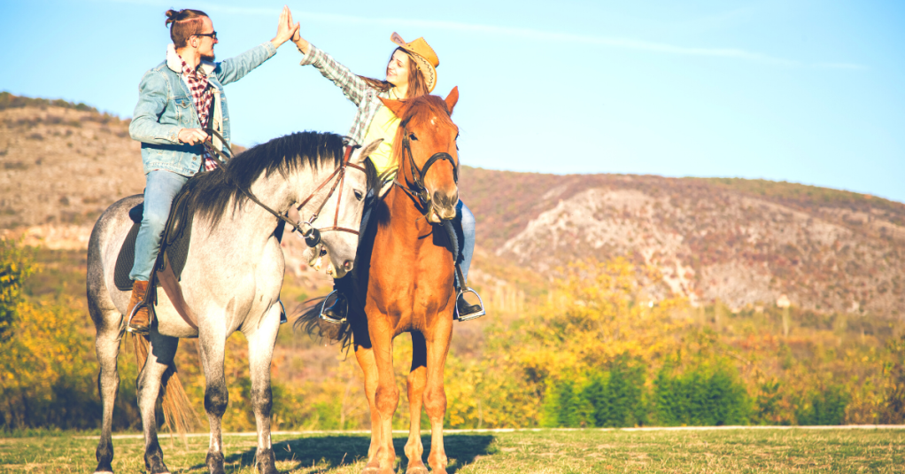couple giving high five riding horse in the fall